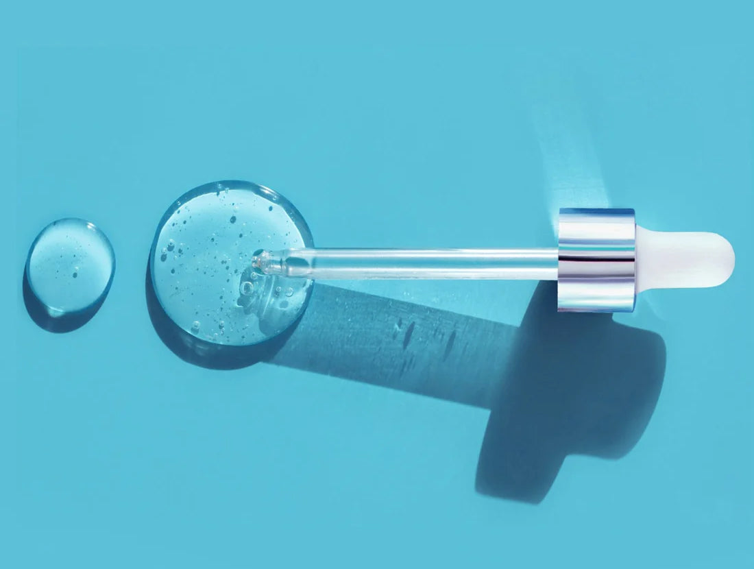 An eyedropper lying on a blue background with 2 drops of a clear serum. Photo credit: Ekaterina Klishevnik / Getty Images
