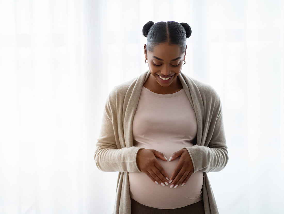 A smiling young pregnant woman looking down and smiling at her hands on her belly. Photo Credit: Prostock-Studio / Getty Images