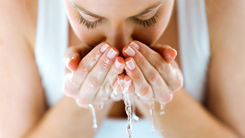Closeup on a woman washing her face, with water dripping from her cupped hands