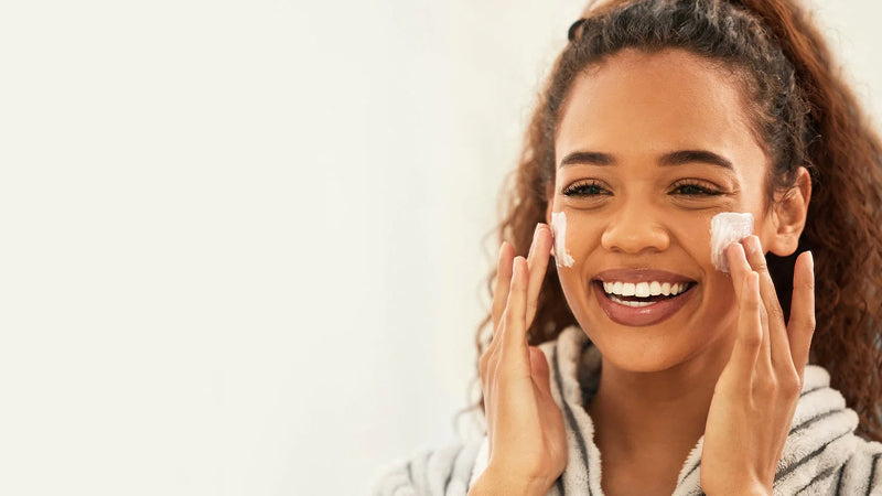 A smiling young woman applying moisturizer to her creeks