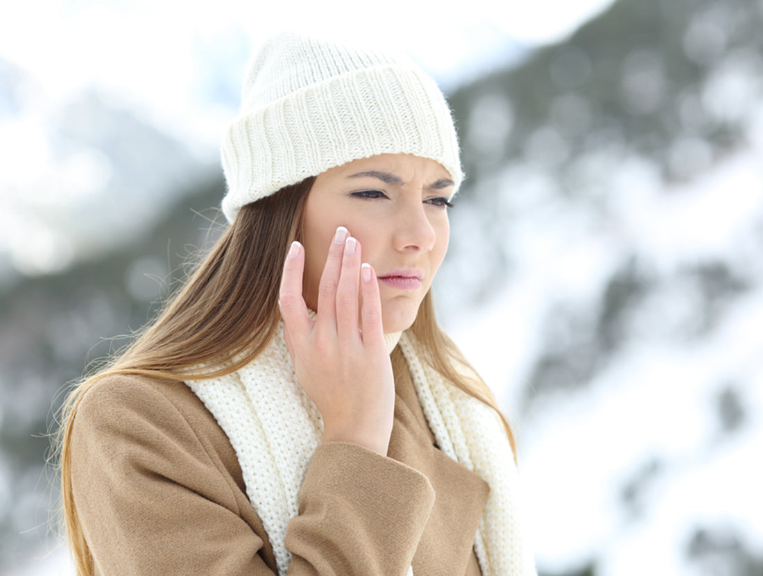 A young woman wearing winter clothes frowns and touches her cheek, with a winter mountain scene in the background. Photo Credit: Antonio Guillem/ Getty Images