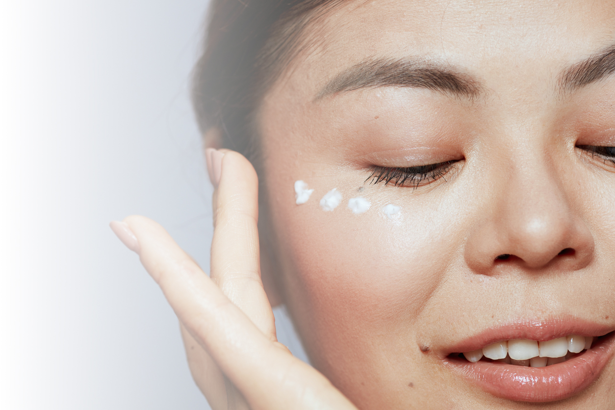 Closeup on a young woman's face as she applies a white cream to the skin under her eye.