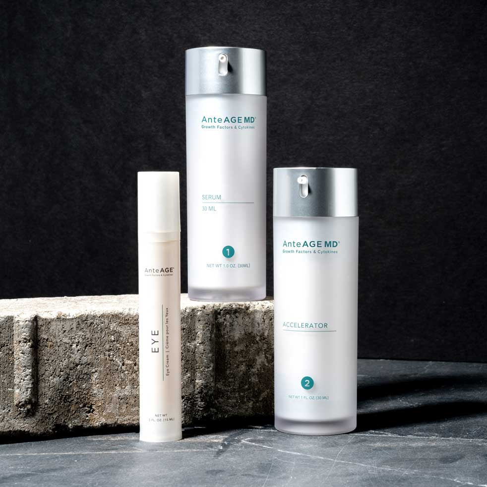 Three AnteAGE MD products (serum, accelerator, and eye cream) standing on a paving stone with a black background