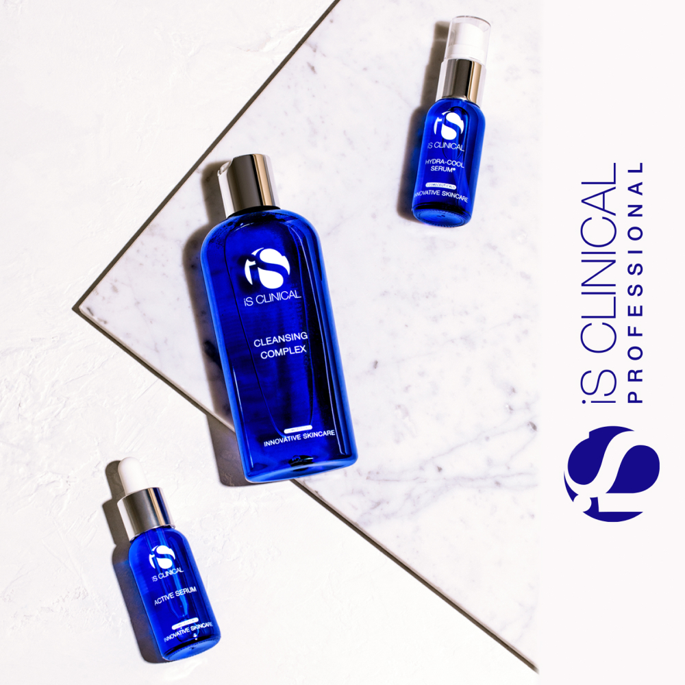 Three blue iS Clinical product bottles (active serum, cleansing complex, and Hydra-Cool serum) lying down on a stone background