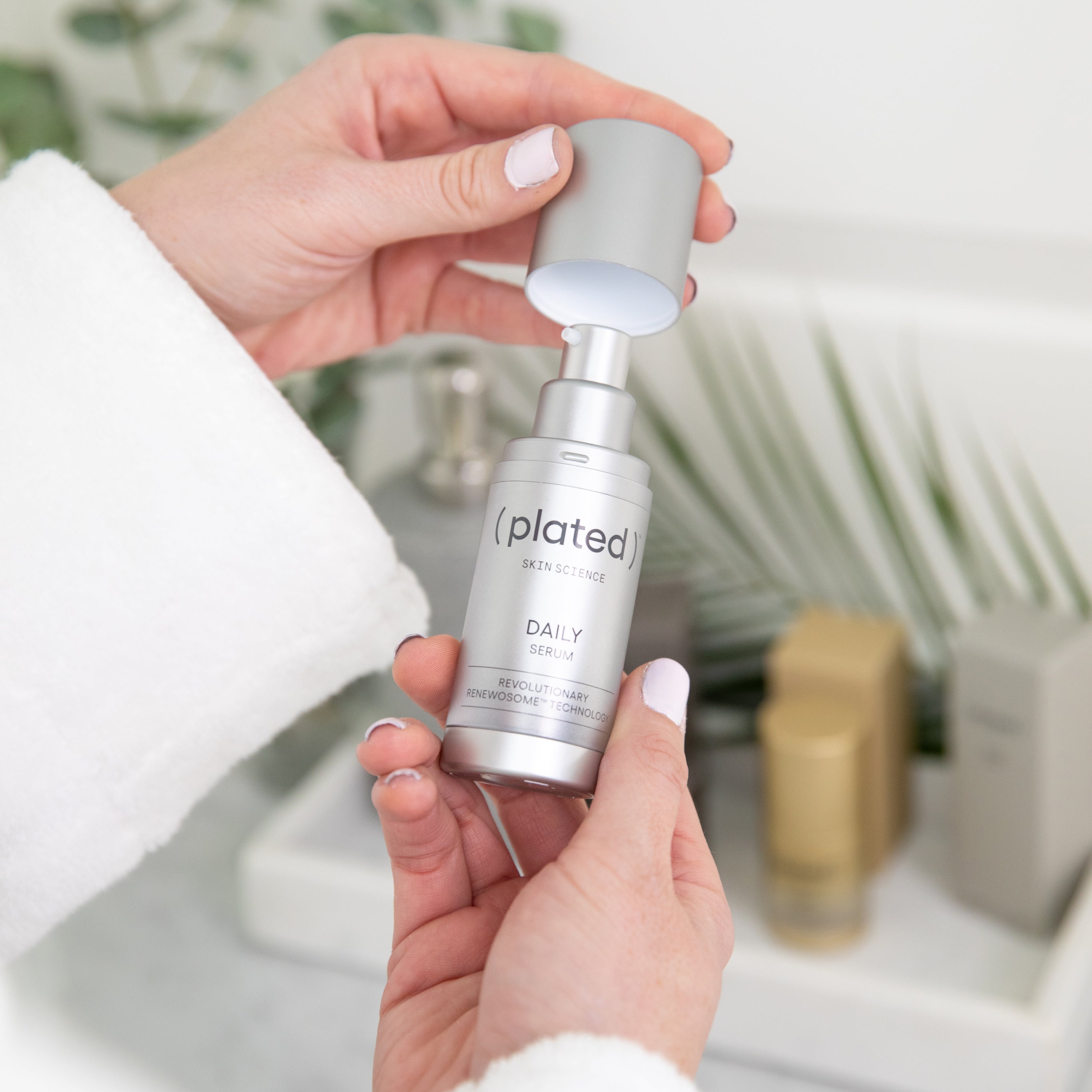 A bottle of Plated Skin Science Daily Serum in the hands of a person wearing a white bathrobe, with a bathroom counter in the background