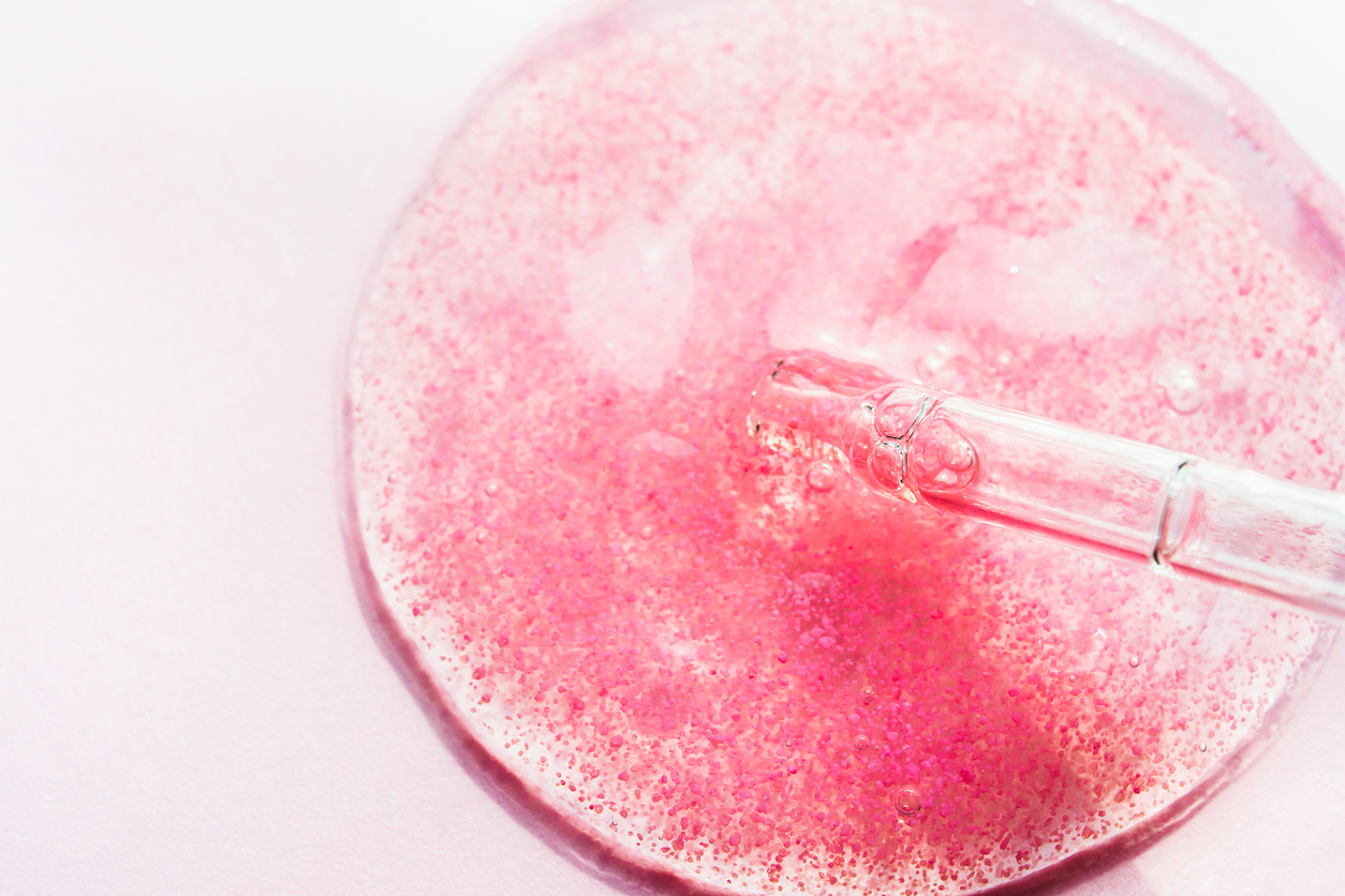 Closeup on a pipette dropping out a small pool of pink serum