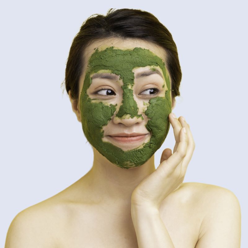 Woman touching the dried green facemask applied to her face.