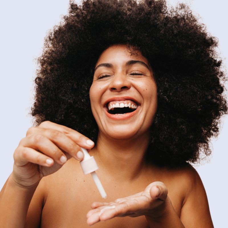 Woman with using a glass cosmetic dropper to apply a serum to her hands.