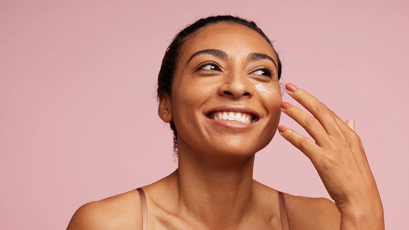 A young woman with nice, clear skin, smiles in front of a pink background