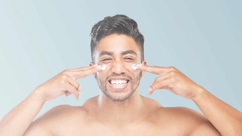 A young man smiles as he applies face cream to his cheeks