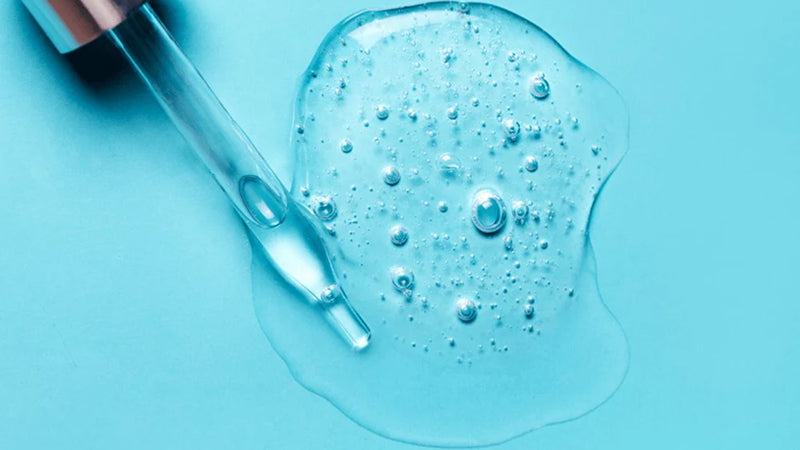 An eye dropper rests on top of a small puddle of hyaluronic acid, a clear serum.