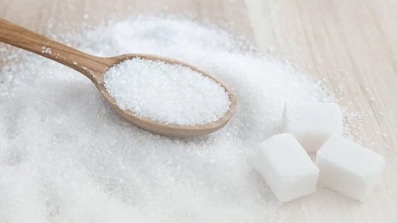Sugar cane crystals, from which glycolic acid is derived, in a pile and in a few cubes on a wooden surface along with a wooden spoon.