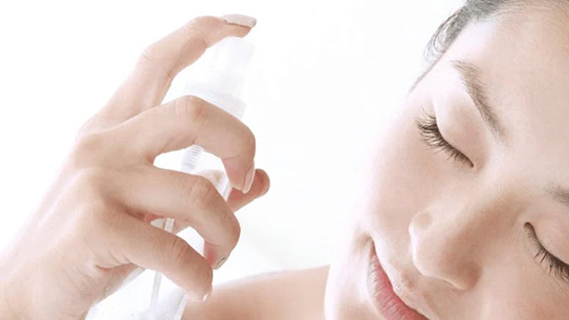 Closeup on a woman spraying product onto her face from a spray bottle