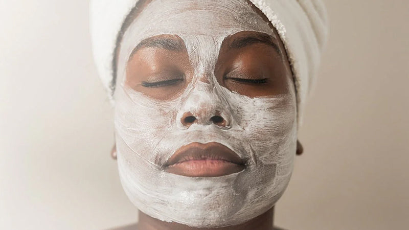 Closeup on the face of a woman relaxing with her eyes closed while wearing a white skincare face mask